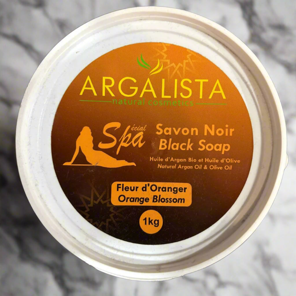 Container of Argalista black soap 1kg with orange blossom background